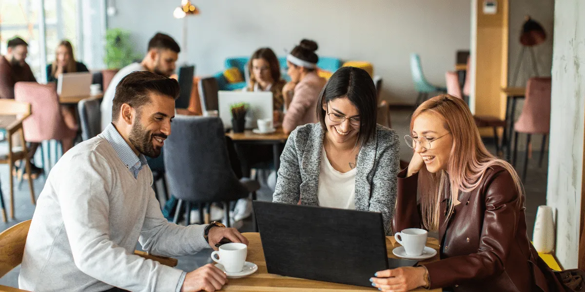 Togetherness in teams, three people sat around laptop drinking coffee