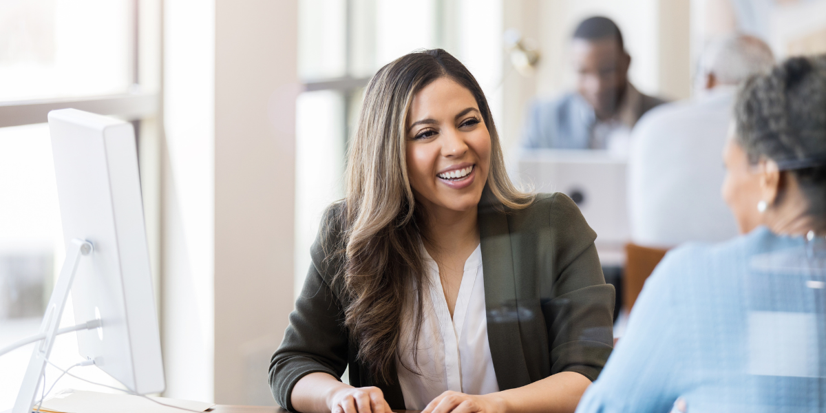 Two happy employees working together at a desk, smiling and talking.