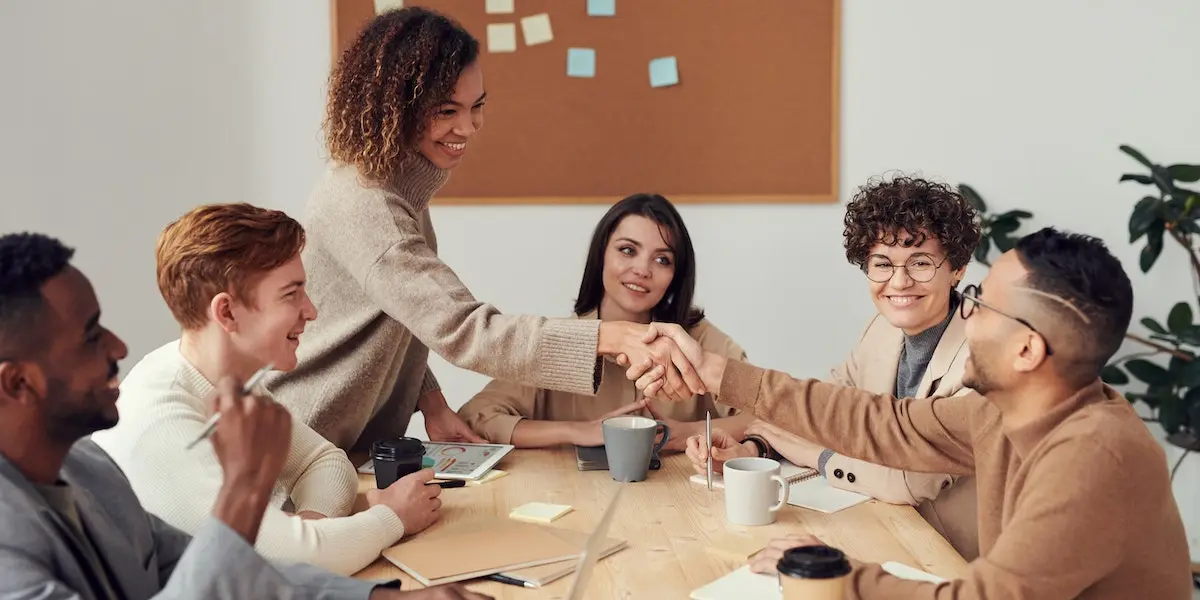 A diverse group of people, laughing and shaking hands, signifying an inclusive workplace.